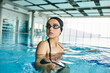 © LIGHTFIELD STUDIOS - A young woman in a swimsuit and goggles gracefully swims in an indoor pool, embodying the essence of tranquility.