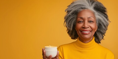 Wall Mural - Smiling senior woman holding a white cream jar, standing against a yellow background.