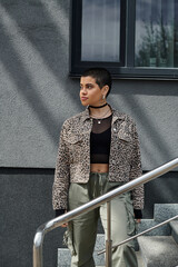 Stylish young woman in leopard print jacket stands on steps of modern building.