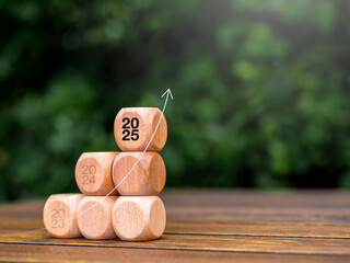 Poster - Rise up arrow on wooden cube blocks stack, business growth graph steps with 2025 year number on wood table on green leaves background with copy space. Green business growing and environment concept.