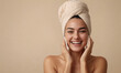 © Qeeraw - Portrait of beautiful smiling woman wearing a bath towel oh her head and touching her clean perfect skin removing makeup with sponges against beige background. Skincare routine, spa treatment