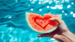 © Creativision - hand holding a watermelon slice with a heart inside at summer pool background
