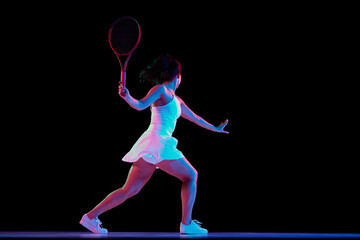 Back view shot of woman in white tennis dress performs forehand shot in neon light against black studio background. Concept of professional sport, championship, active lifestyle, tournament. Ad