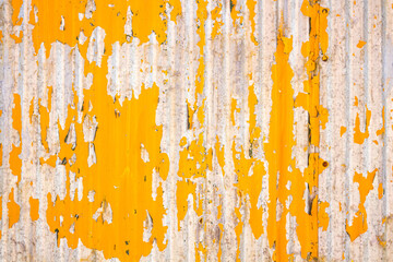 Close up of a weathered corrugated metal surface with peeling yellow paint, revealing rust and wear underneath.