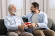 © New Africa - Son giving gift box to his dad on sofa at home