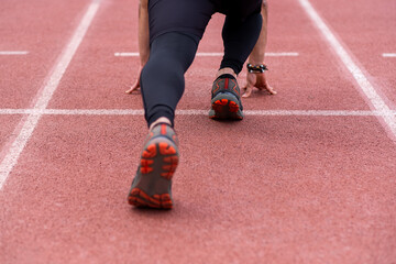 Focused on the legs of a professional sportsman in a starting position, poised to run along the vibrant red rubberized track at an outdoor stadium, ready for an exhilarating workout