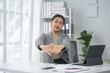 © amnaj - Woman stretching at her desk in a modern office setting, taking a break from work on her laptop, appearing relaxed and content.