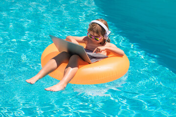 Wall Mural - Summer travelling. Funny little businessman freelancer relaxing in the pool, using laptop computer in summer water. Child online working on tropical sea. Freelance work concept.