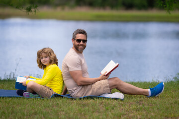 Aufkleber - Lovely family reading a book on grass. Boy and dad having a picnic in park. Happy son and father reading a book. Happiness family. Father reading a book to child sitting outdoor on the grass in park.