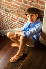 Wall Mural - Portrait of a young boy sitting on stairs looking up at the camera with a curious expression	