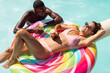 © Wavebreak Media - A diverse couple relaxing on colorful pool float, enjoying drinks