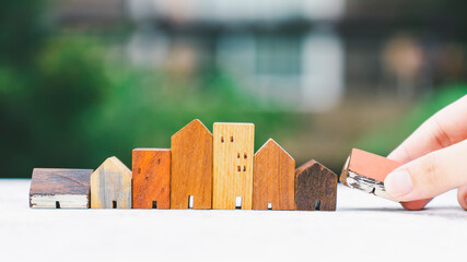 Wall Mural - Hand choosing mini wood house model from model on wood table, selective focus, Planning to buy property. Choose what's the best. A symbol for construction ,ecology, loan concepts	