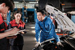 © tigercat_lpg - Asian male professional automotive engineer supervisor describes car engine maintenance and repair work with mechanic worker staffs team in fix service garage, specialist occupations in auto industry.