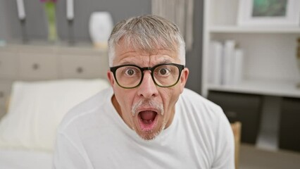 Wall Mural - Amazed middle-age, grey-haired man in pyjamas, shocked and afraid in his bedroom, displaying an expression of shock, fear and excitement on his face