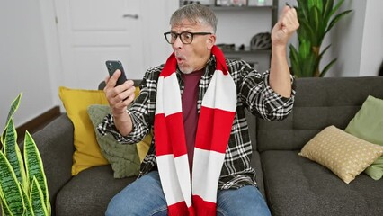 Canvas Print - Middle-aged, grey-haired man in shock! amazed and scared, mouth open, scarf-clad senior can't believe what's on his home smartphone screen!