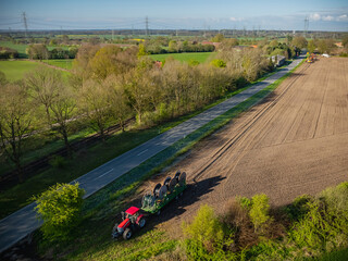 Tractor pulling a trailer with four wire spools, cable drums. Deploying cables or wires over larger distances.  Installing optical fiber cables along trench. Rolling out fiber optic cables for network