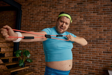 Comic chubby man in sportswear fooling around with fitness equipment