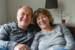 © Victor Bertrand - A happy older couple sitting close together on a couch, smiling warmly and embracing each other in a cozy home setting.