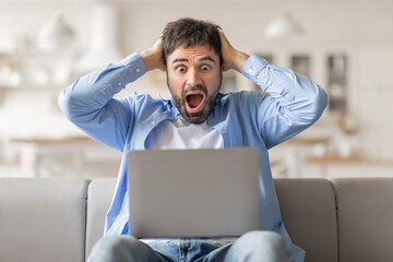 Poster - Man sitting on a couch, staring in shock at his laptop screen. His hands are on his head, and his mouth is open in surprise. He appears to be reacting to something he has just seen on the screen