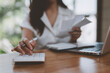 © Phimwilai - Woman working outside using calculator and laptop Attentive Asian woman checks taxes, rent, financial expenses to pay bills Control your finances online Accounting work concept.