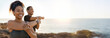© Prostock-studio - African American woman and man are stretching their arms in front of a beautiful sunset view over the ocean. They are standing on a rocky cliff, with the ocean stretching out behind them, copy space