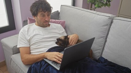 Poster - A man relaxes on a sofa with a laptop and a siamese cat, depicting a cozy indoor setting.