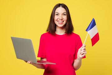 Wall Mural - Young smiling happy cheerful IT woman wear pink t-shirt casual clothes hold French flag use work on laptop pc computer isolated on plain yellow orange background studio portrait. Lifestyle concept.