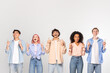 © Prostock-studio - A group of five young adults, each of a different ethnicity and wearing casual clothing, stand in a row and point upwards with their index fingers, copy space