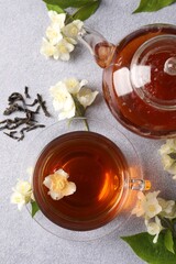 Wall Mural - Hot jasmine tea in cup, teapot and flowers on light grey table, flat lay