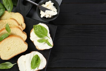 Wall Mural - Pieces of bread with cream cheese and basil served on black wooden table, flat lay. Space for text