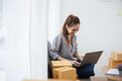 © aksonsat - Owner SME Small and Medium Enterprises woman received orders from clients laptop then writing preparing products in parcel cardboard box packaging at home ready for delivery to customer