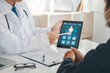 © Antony Weerut - Medicine, healthcare and people concept. A doctor is showing a patient's medical record on a digital tablet. The patient is looking at the screen and listening to the doctor. Results for health.