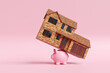 © Dragon Claws - Detached house with a garage on the back of a pink piggy bank on pink background. Illustration of the on concept of increasing interest rate, debt burden of mortgage loan and rising cost of living