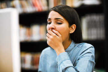 Poster - Tired, student and woman with computer, yawning and exhausted with deadline, overworked and burnout. Education, university and girl with fatigue, stress and studying for exams and sleepy in library