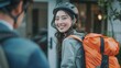 © ifoto - A smiling young Asian woman receiving her food delivery from a male rider wearing a helmet and orange backpack