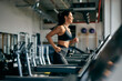 © bnenin - Side profile of a smiling fit woman running on a treadmill at the gym.