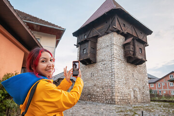 Wall Mural - A happy young woman capturing memories with her smartphone in front of Kula Redzepagica, a historic landmark in Montenegro, Plav