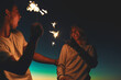 © JorSons/peopleimages.com - Night, couple and playing together with sparklers for healthy relationship and romantic love with trust. Firecracker, happy man and woman with smile for anniversary or birthday celebration in Bali