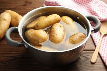 Wall Mural - Raw potatoes in pot with water on wooden table