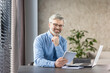 © Liubomir - Confident office professional with glasses using tablet while working remotely in a stylish home office setting. Bright and modern workspace with a positive work atmosphere.