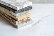 © artitwpd - A variety of marble and quartz countertop samples are stacked on a white marble background.