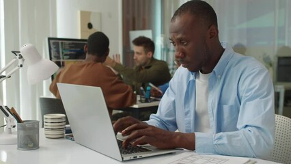 Medium shot of serious male coder testing application on wireless laptop while working at office table