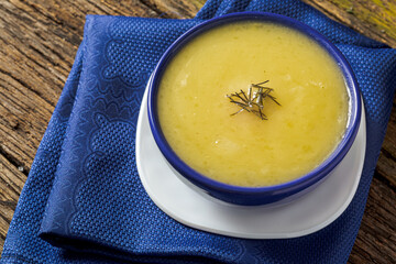 Delicious cassava cream (Caldo ou Creme de Mandioca) or cassava soup, typical of Brazilian cuisine, served in a blue porcelain bowl, on top of a typical rustic farm table, top view with selective focu