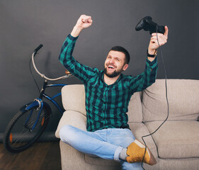 young hipster handsome bearded man sitting on couch at home, playing video game