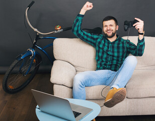 young hipster handsome bearded man sitting on couch at home, playing video game