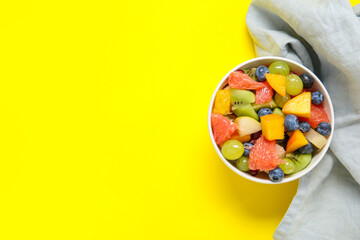 Wall Mural - Bowl with fresh fruit salad on yellow background