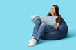 © Pixel-Shot - Shocked young woman in beanbag chair with newspaper on blue background