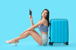 © Pixel-Shot - Beautiful young happy female tourist with suitcase, passport and ticket sitting on blue background