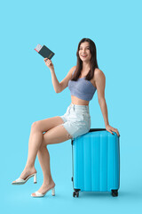 Poster - Beautiful young happy female tourist with suitcase, passport and ticket on blue background