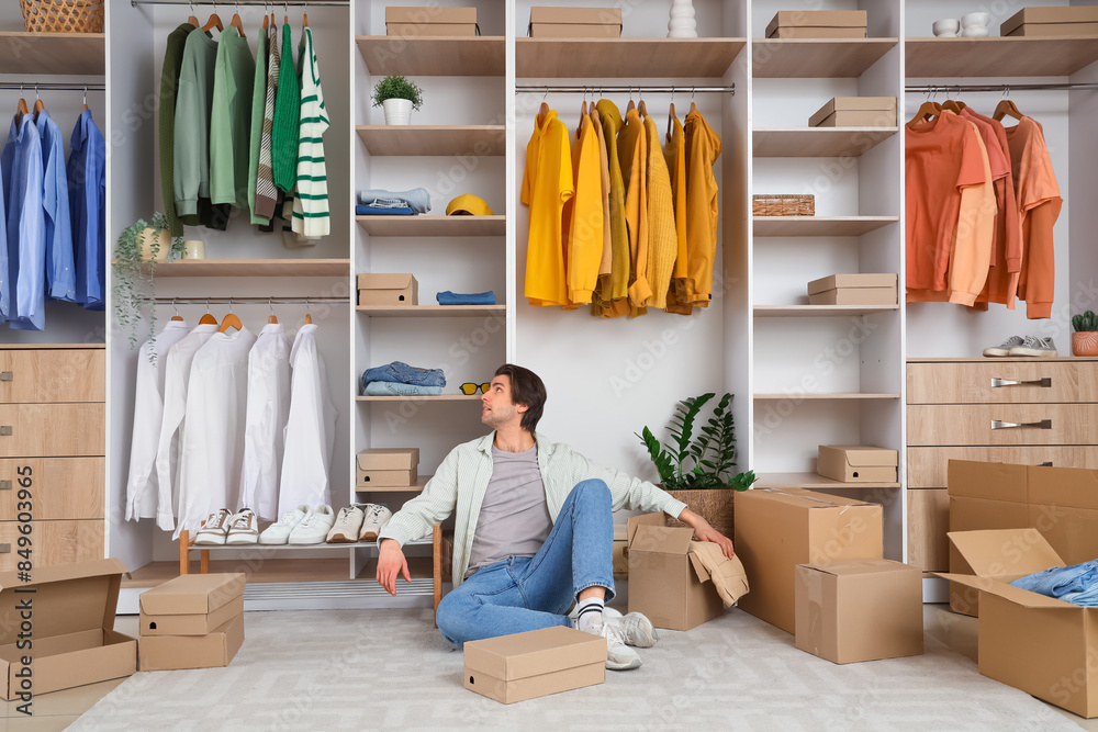 Handsome young tired man with wardrobe boxes and stylish clothes in dressing room